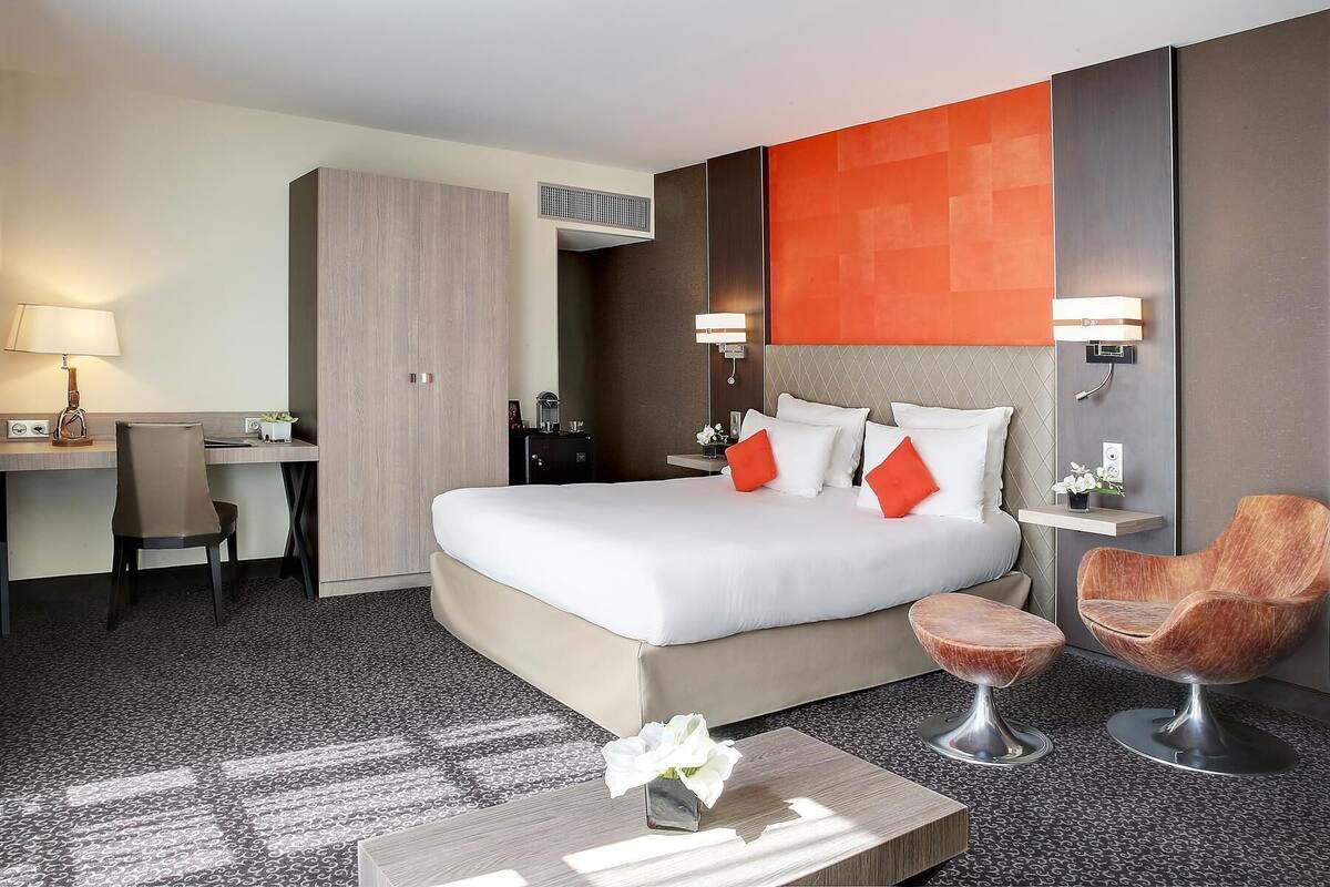 Hotellihuone, jossa on sänky, työpöytä, tuoli ja kaksi nojatuolia.