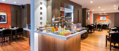 A breakfast buffet with various food items, a seating area with tables and chairs, and a wall-mounted television.