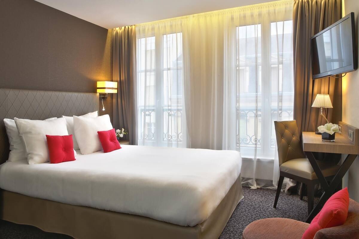 Hotellihuone, jossa on suuri sänky, työpöytä lampun kanssa, televisio ja tuoli.