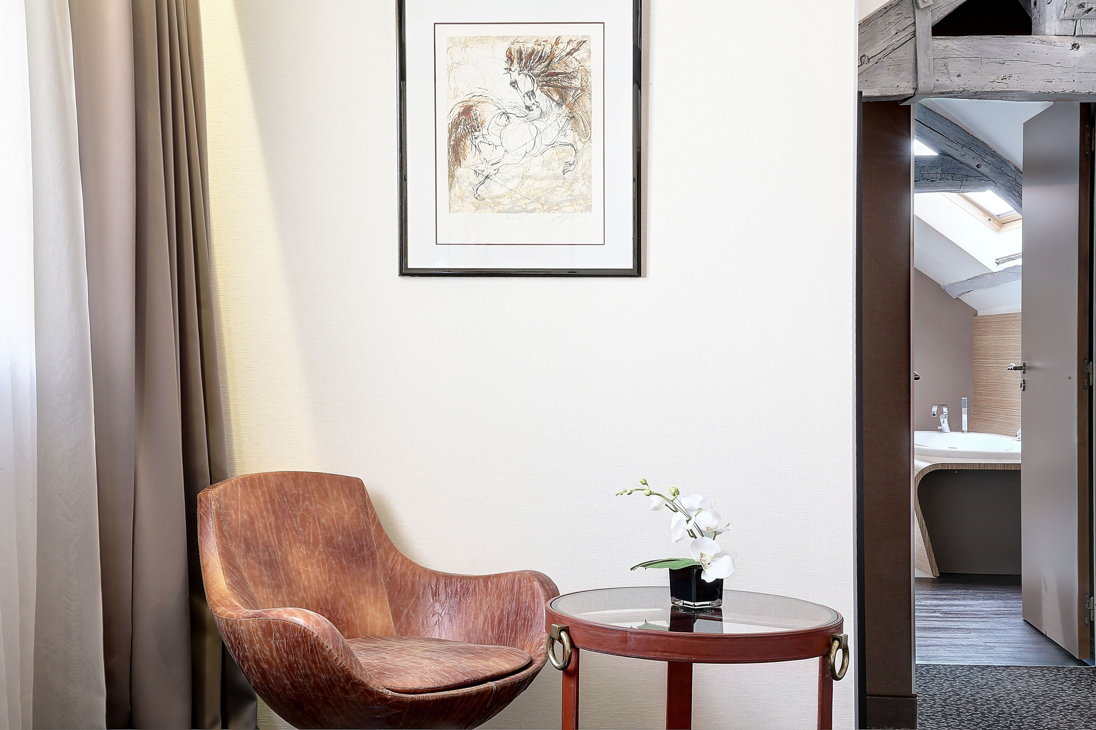 Una habitación con una silla de madera, una mesita con un jarrón de flores y una obra de arte enmarcada en la pared.