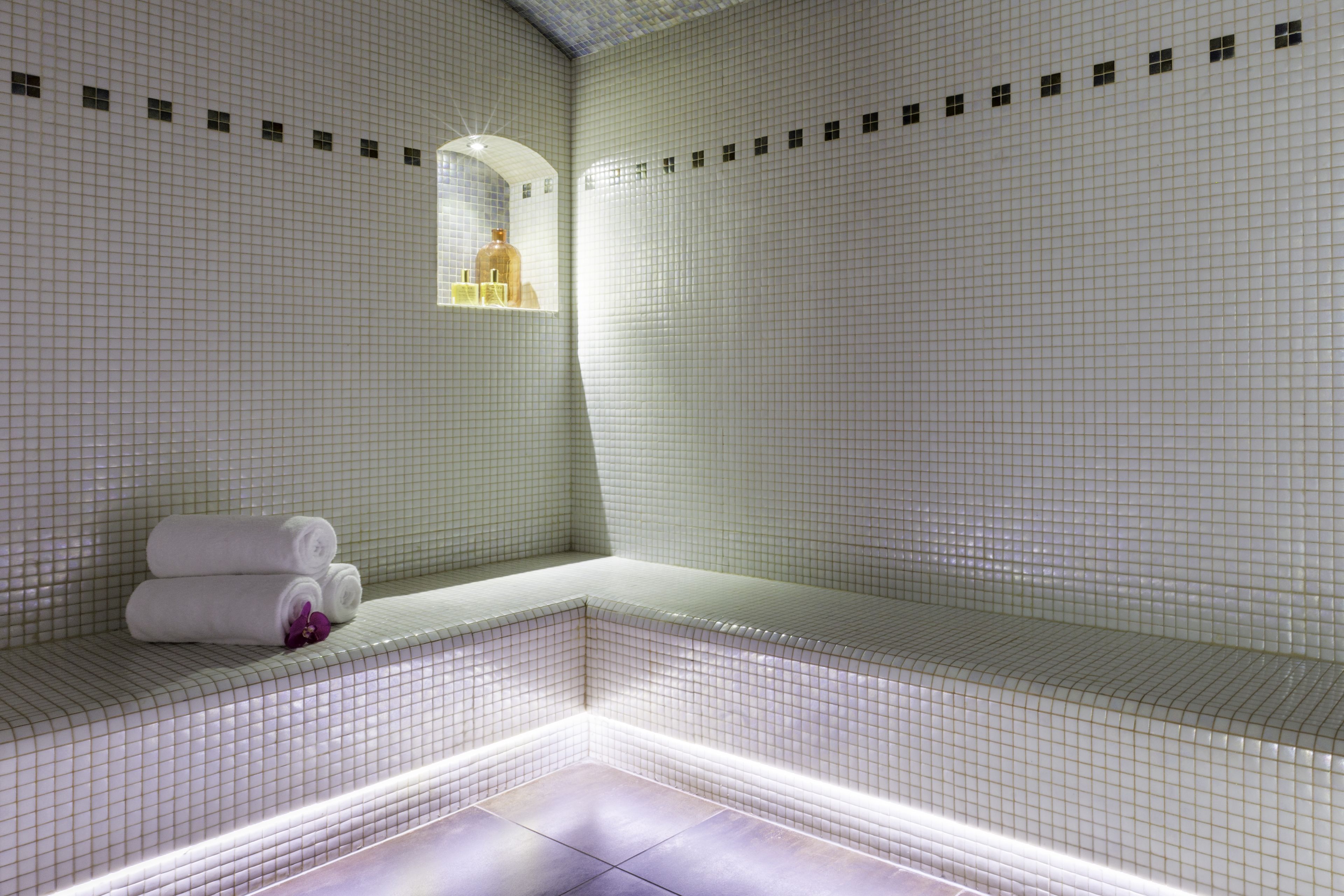 A tiled bathroom with a bench, a mirror, and a shelf with toiletries.