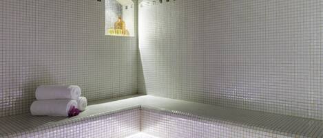 A tiled bathroom with a bench, a mirror, and a shelf with toiletries.