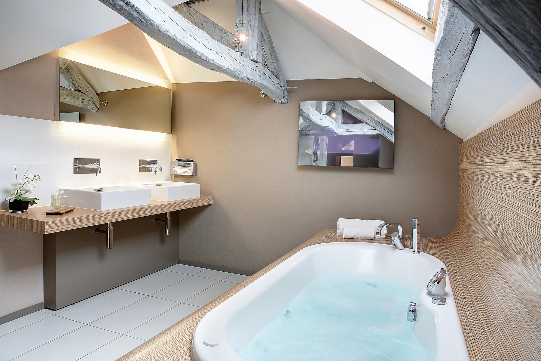 A modern bathroom with a skylight, two sinks, a bathtub, and a large mirror.