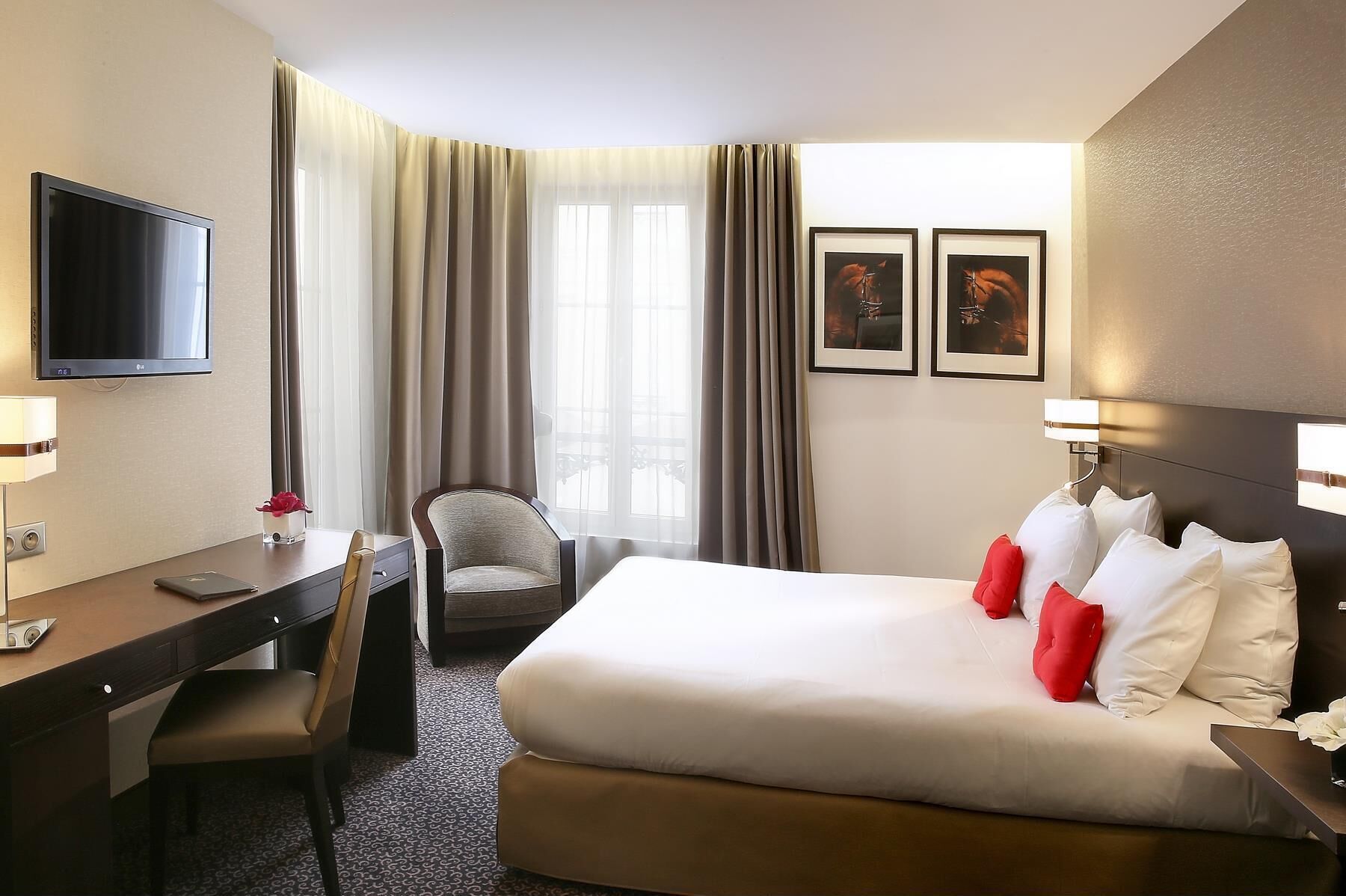 A hotel room with a bed, desk, chair, TV, and two framed pictures on the wall.