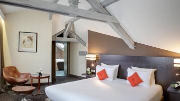 A hotel room with a large bed, a wooden chair, a small table, and a framed picture on the wall.