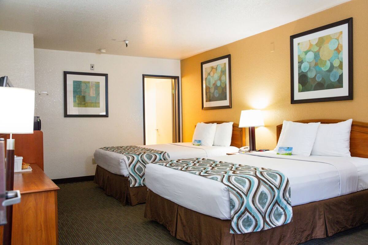 A hotel room with two beds, a desk, and artwork on the walls.