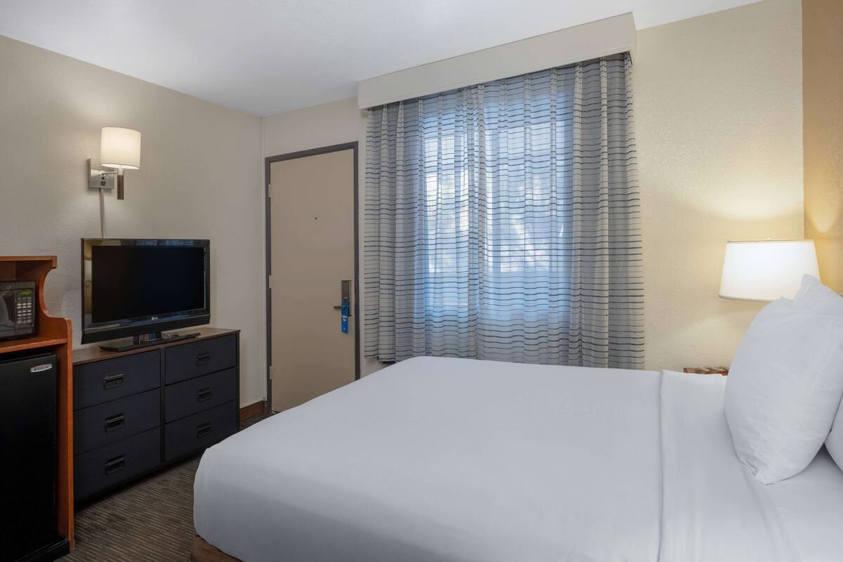 A hotel room with a bed, a television on a dresser, a door, and curtains.