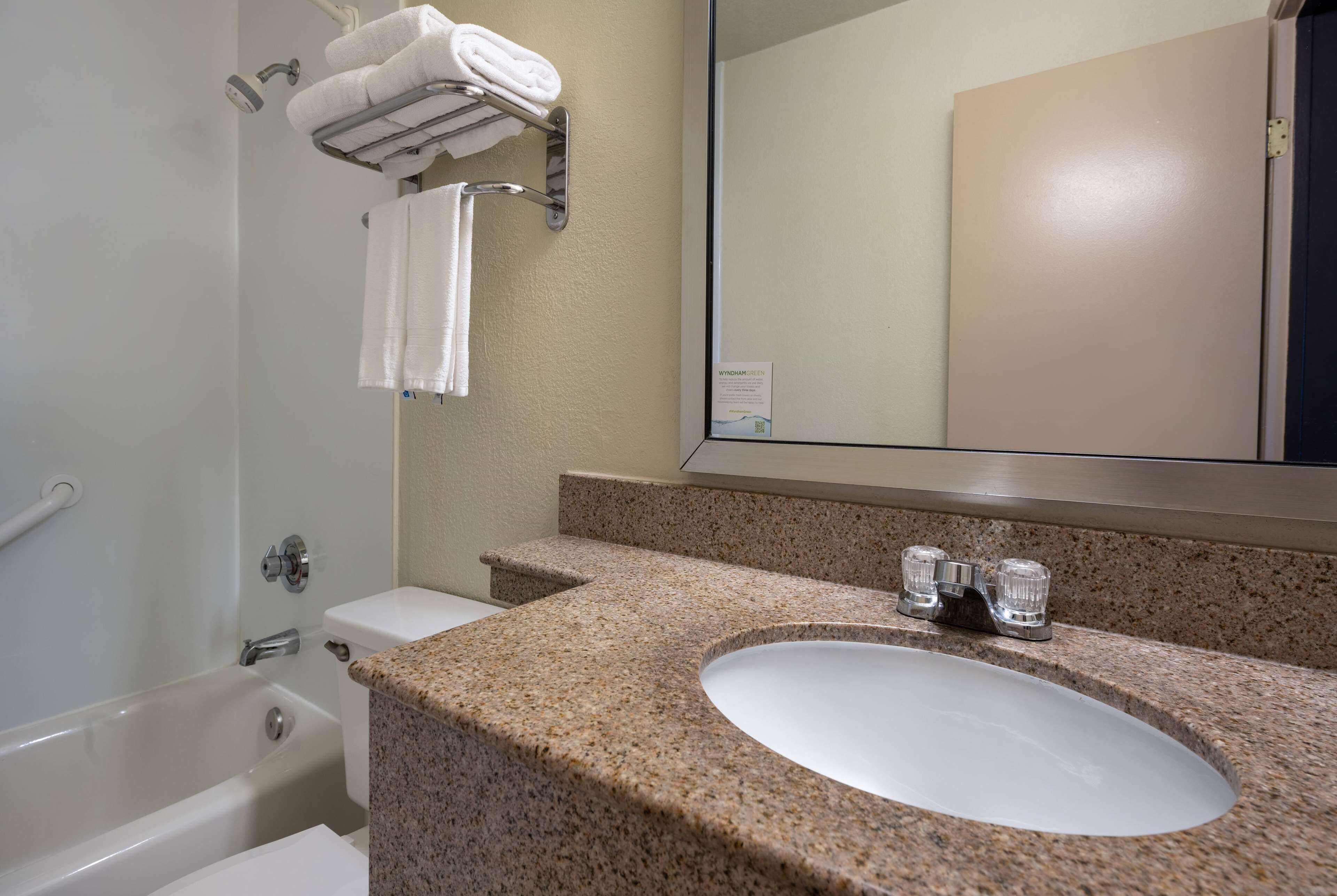 A bathroom with a granite countertop sink, a large mirror, a towel rack, and a bathtub.