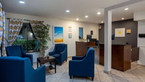A hotel lobby with blue armchairs, a reception desk, and a large window with curtains.