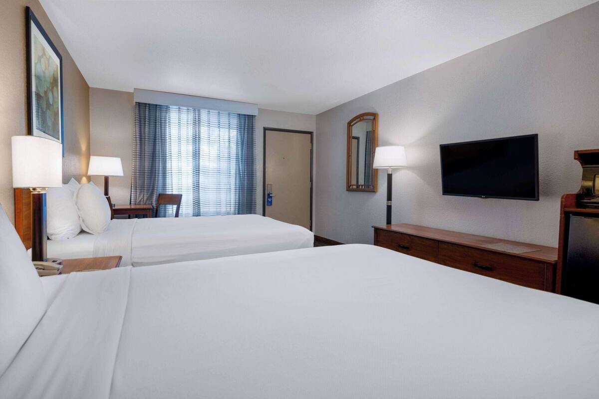 A hotel room with two beds, a television, a desk with a lamp, and a window with blinds.