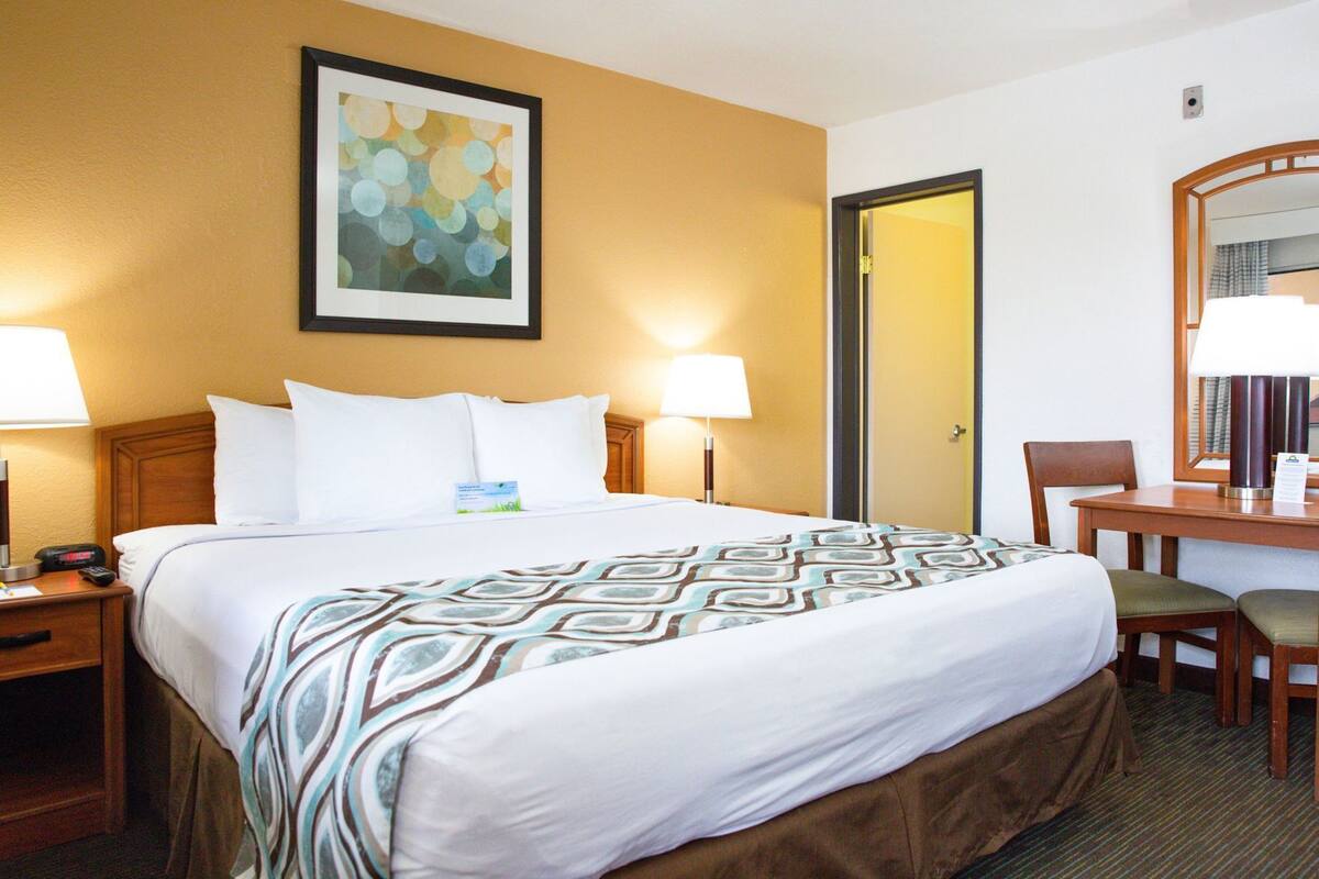 A hotel room with a bed, bedside lamps, a desk, and a chair.
