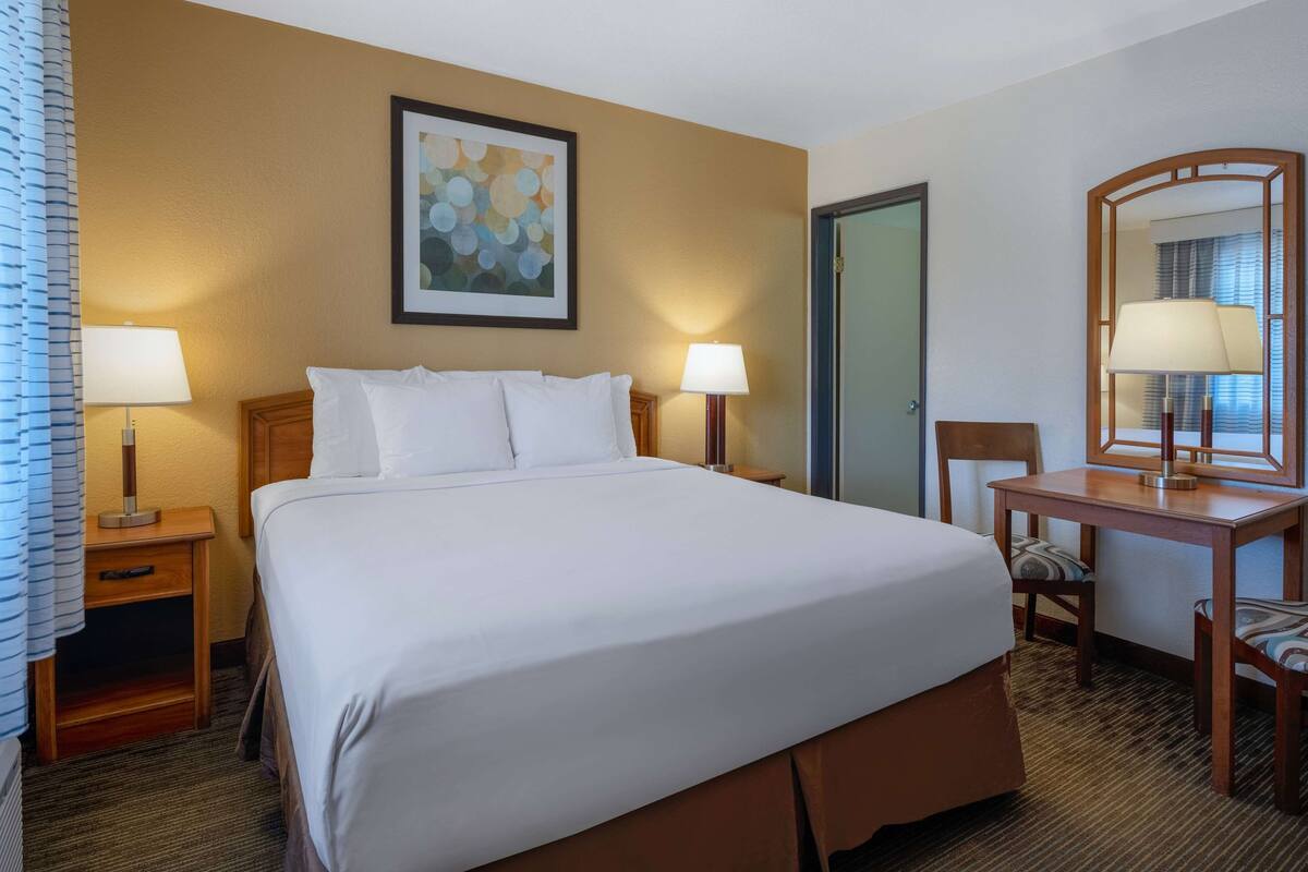 A hotel room with a large bed, two bedside tables with lamps, a desk with a chair, and a door.
