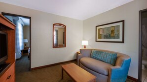 A hotel room with a sofa, a wooden table, a mirror, a lamp, and a framed picture on the wall. - Days Inn by Wyndham Encinitas Moonlight Beach (Encinitas)