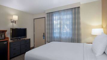 A hotel room with a bed, a television on a dresser, a desk, and a door.