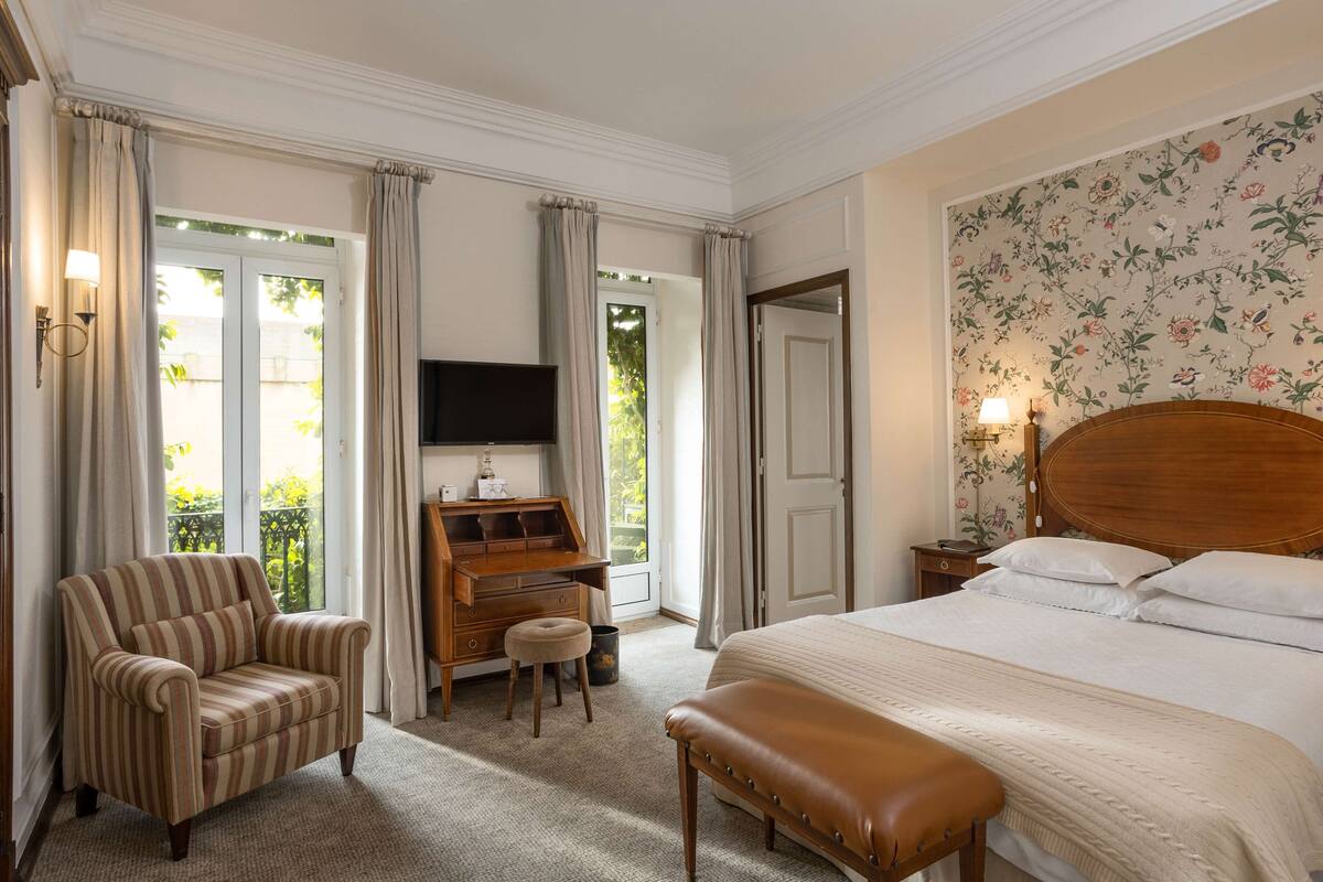 Una habitación de hotel con una cama, un escritorio, una silla, un banco y un televisor.