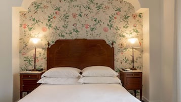 A bedroom with a floral wallpaper, a wooden headboard, two bedside tables with lamps, and a bed with white linens.