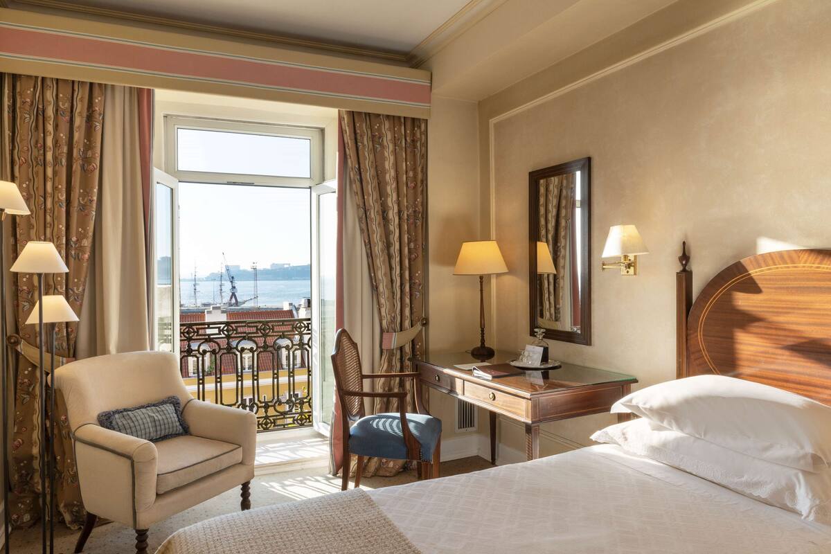 Habitación de hotel con cama, escritorio, silla y vistas a la ciudad a través de la ventana.