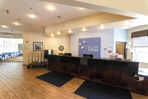 A hotel reception area with a wooden floor, a reception desk, a clock, and a wall-mounted sign for Holiday Inn Express.