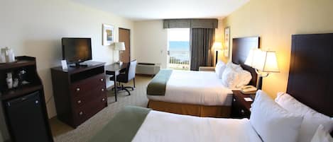 A hotel room with two beds, a desk, a television, a mini-fridge, and a view of the ocean.