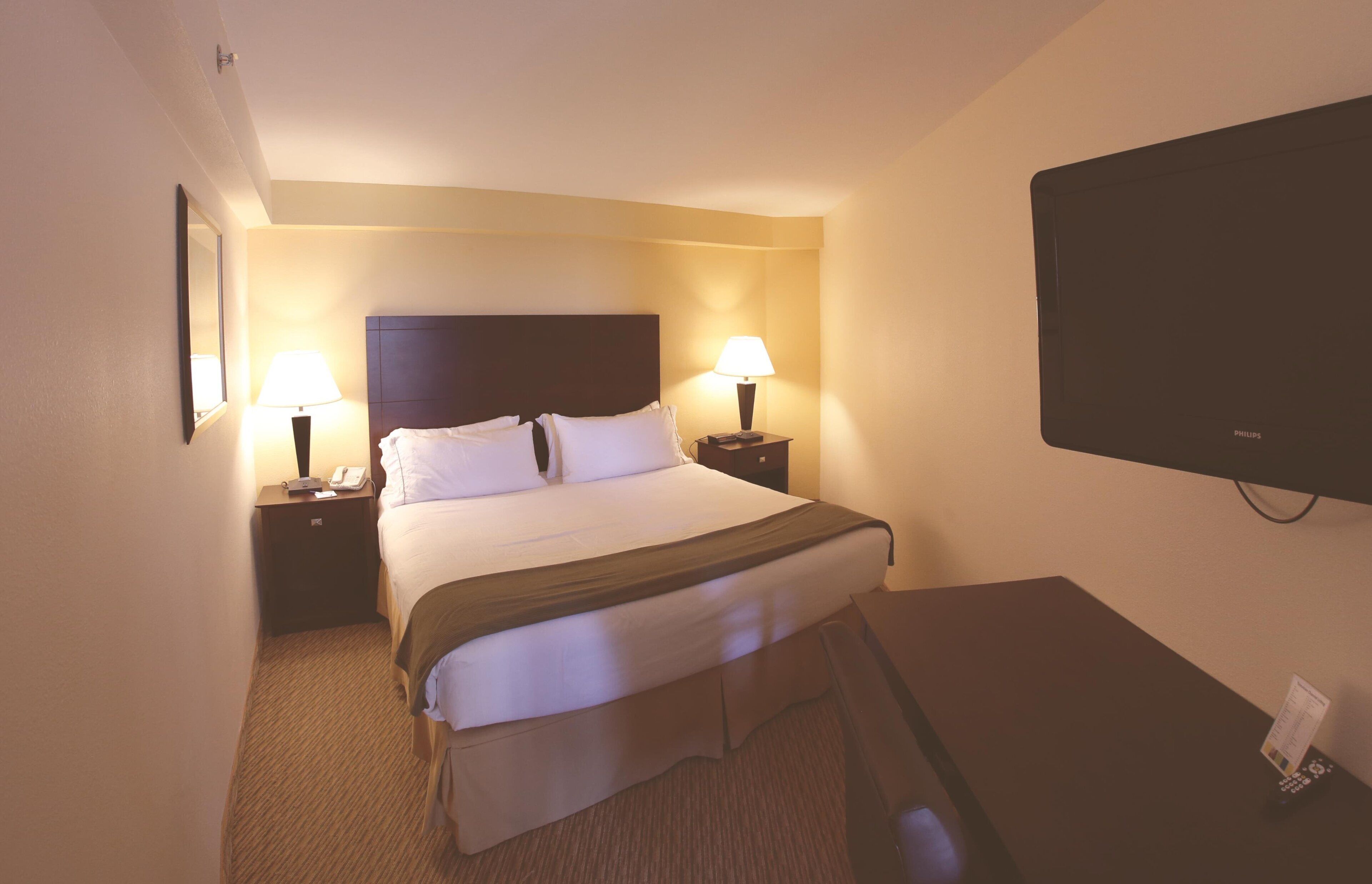 Une chambre d’hôtel équipée d’un lit, de lampes de chevet, d’un téléviseur à écran plat et d’un bureau avec un téléphone.