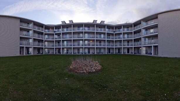 A multi-story building with a curved facade, balconies, and a central courtyard with grass and a small plant bed. - Holiday Inn Express St. Ignace-Lake Front by IHG (St Ignace)