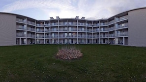 A multi-story building with a curved facade, balconies, and a central courtyard with grass and a small plant bed. - Holiday Inn Express St. Ignace-Lake Front by IHG (St Ignace)
