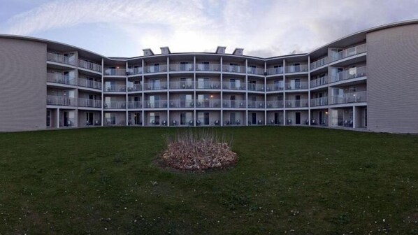 A multi-story building with a curved facade, balconies, and a central courtyard with grass and a small plant bed. - Holiday Inn Express St. Ignace-Lake Front by IHG (St Ignace)