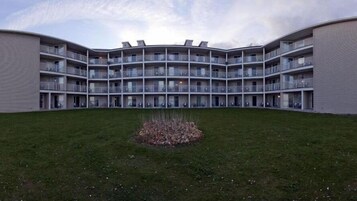 Un edificio de varios pisos con fachada curva, balcones y un patio central con césped y un pequeño macizo de plantas.