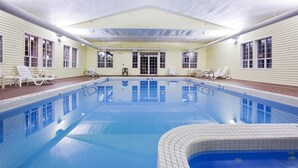 A large indoor swimming pool with clear blue water, surrounded by lounge chairs and a covered seating area.