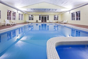 A large indoor swimming pool with clear blue water, surrounded by lounge chairs and a covered seating area.