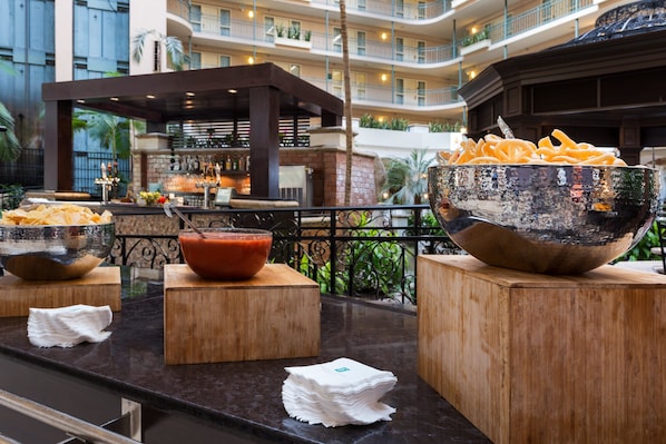 Montaje tipo bufé con fuentes de comida y una zona de bar en el vestíbulo de un hotel.