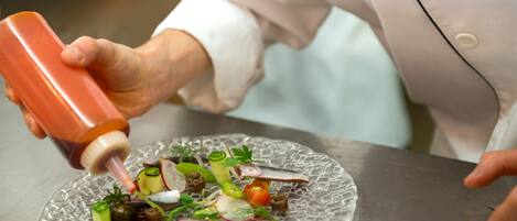 A chef preparing a dish with a variety of vegetables and fish on a glass plate.