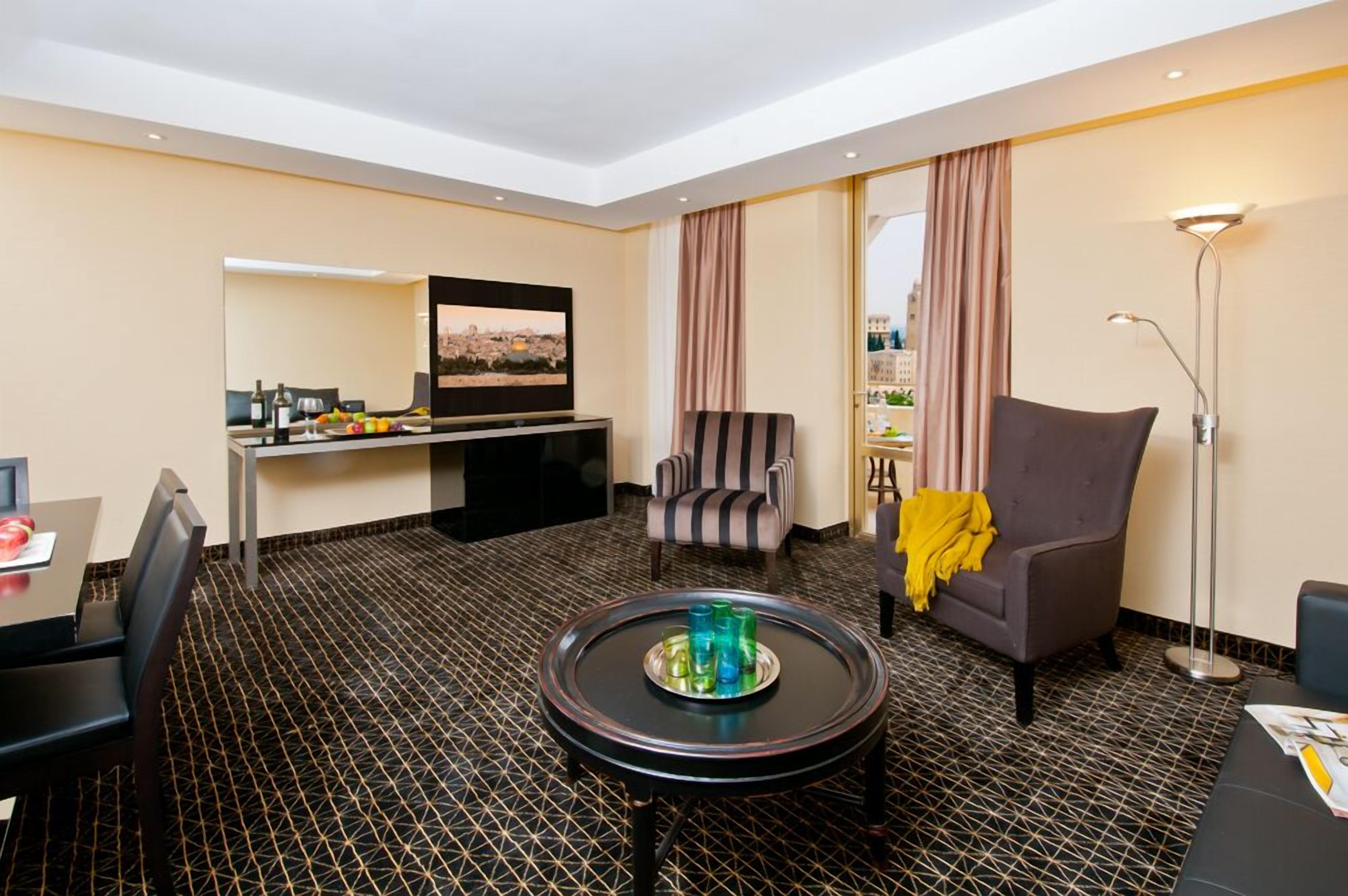 Habitación de hotel con una mesa de comedor, un sofá, un televisor y un suelo de diseño geométrico.