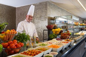 Un bufé con diversos alimentos y un cocinero con uniforme.