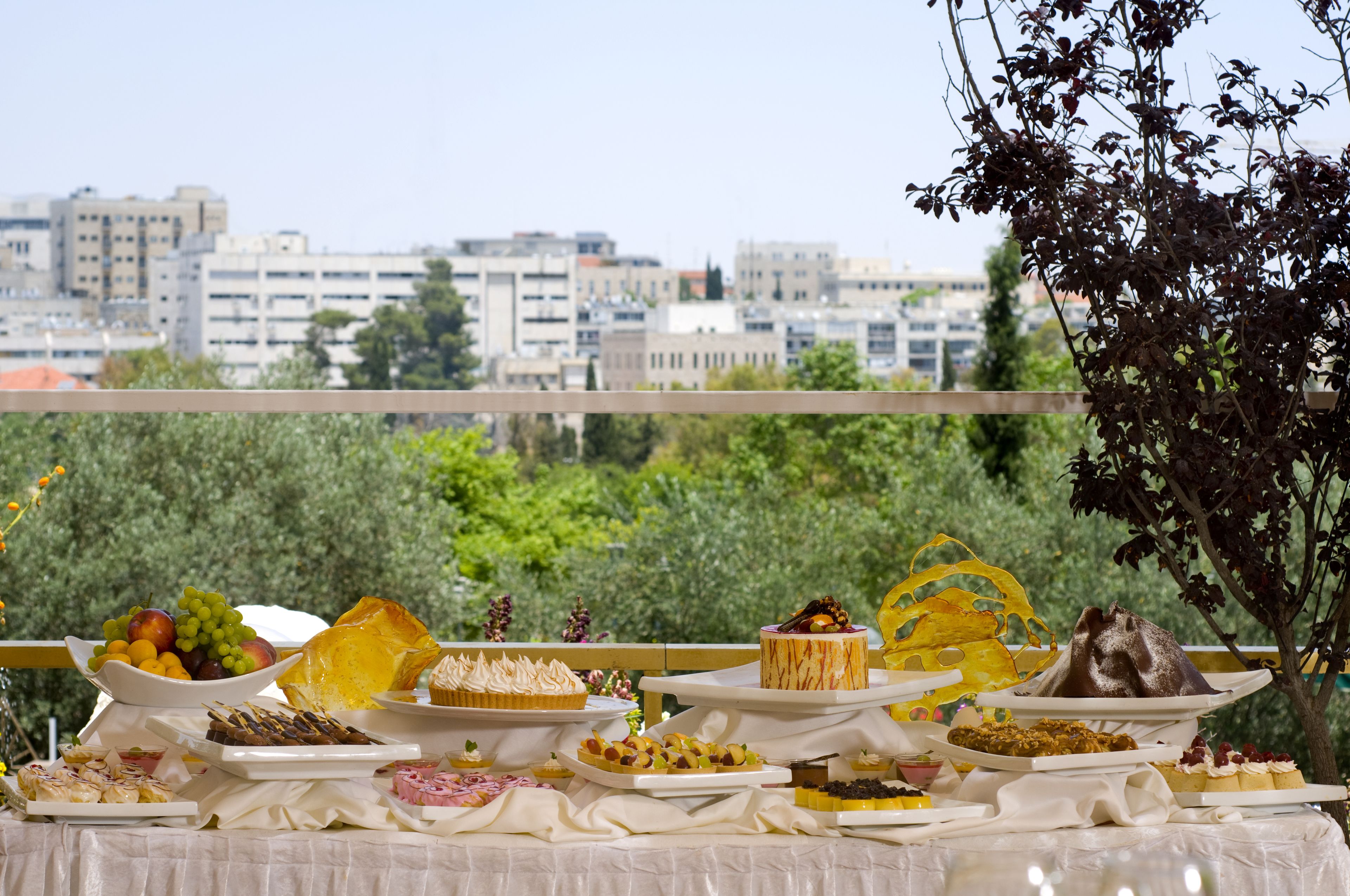 Una mesa de buffet con diversos alimentos y un paisaje urbano al fondo.