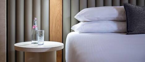 A hotel room with a bed, a round table with a bottle and glass, and a wall with vertical panels.
