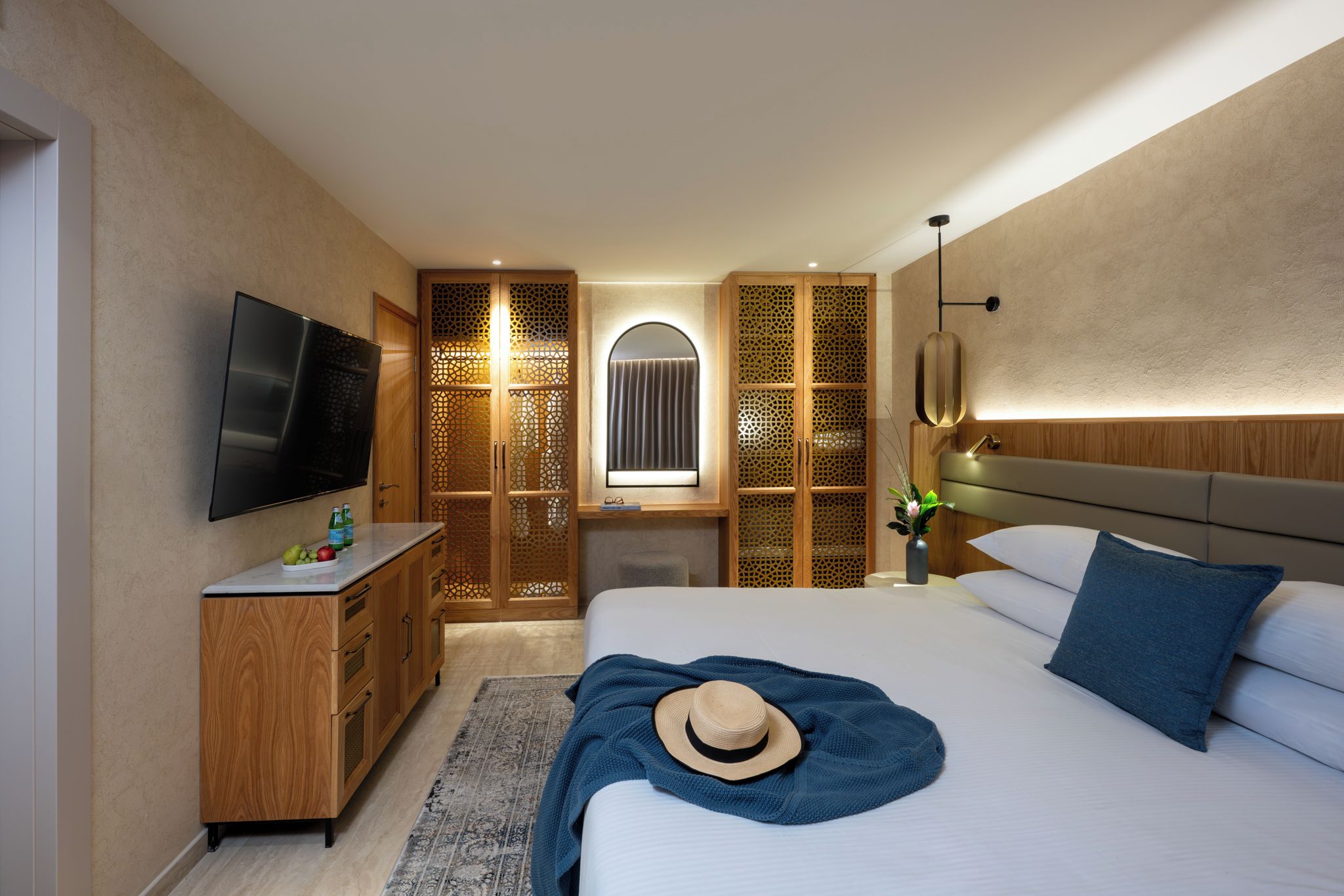 Ein modernes Hotelzimmer mit einem großen Bett, einem Fernseher, einem Holzschrank und einem dekorativen Raumteiler.