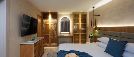 Habitación de hotel moderna con una cama grande, televisor, armario de madera y un separador decorativo.