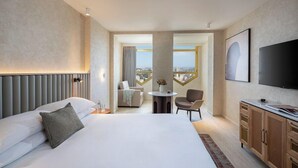 Habitación de hotel con una cama grande, televisión, zona de comedor y vistas a la ciudad.