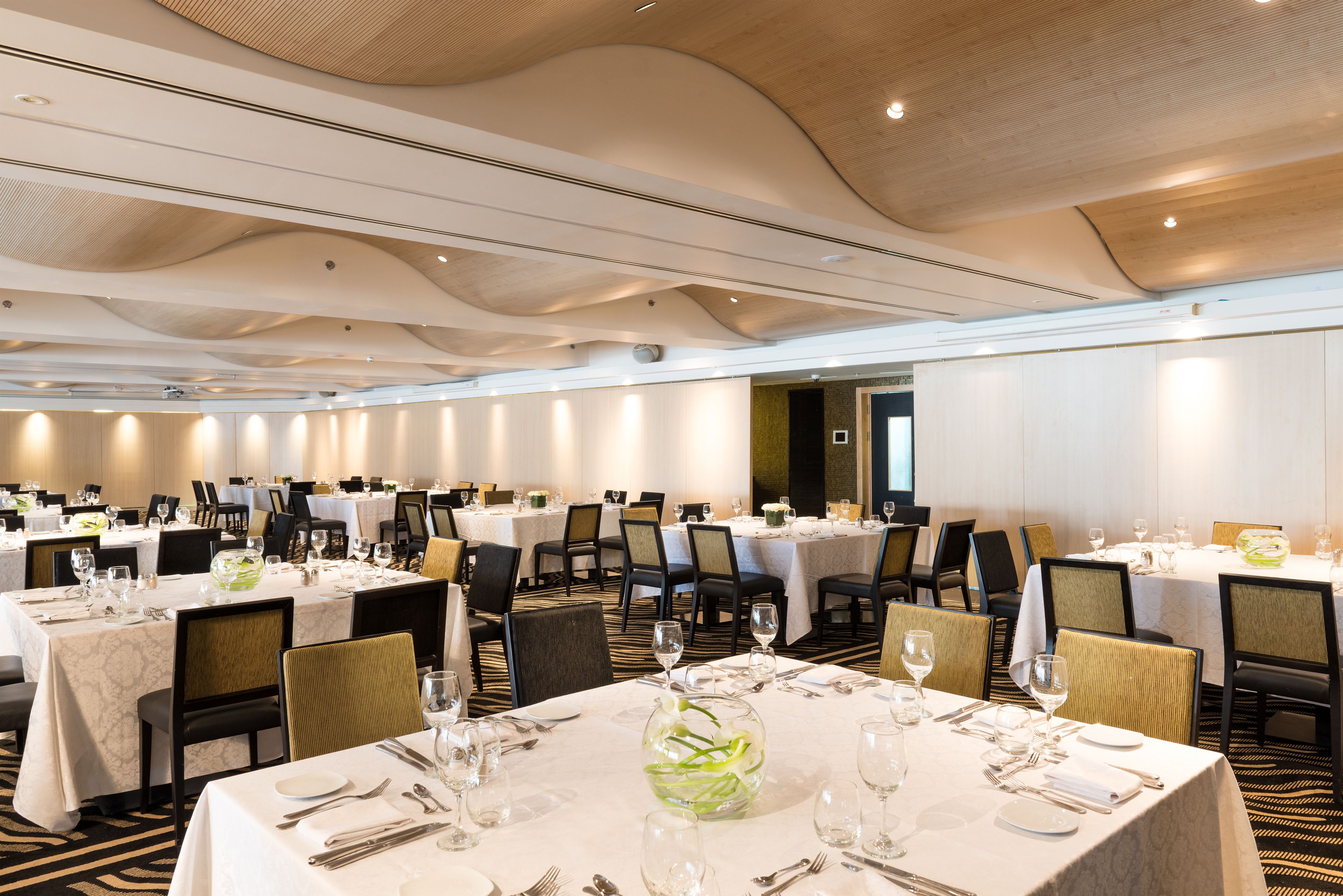 Une grande salle de banquet avec de nombreuses tables rondes dressées pour le repas, ornées de nappes blanches et de verres élégants.
