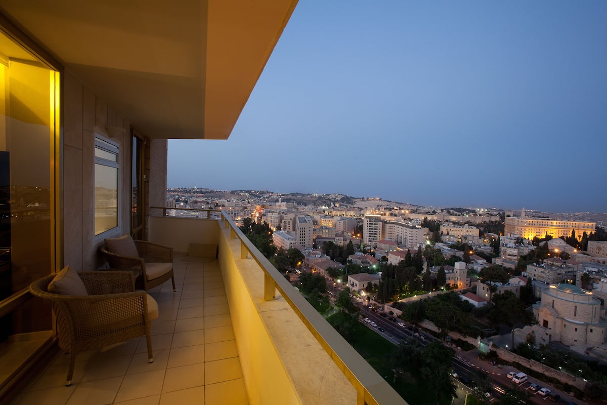 A balcony with wicker chairs, a city view, and a building with illuminated windows.