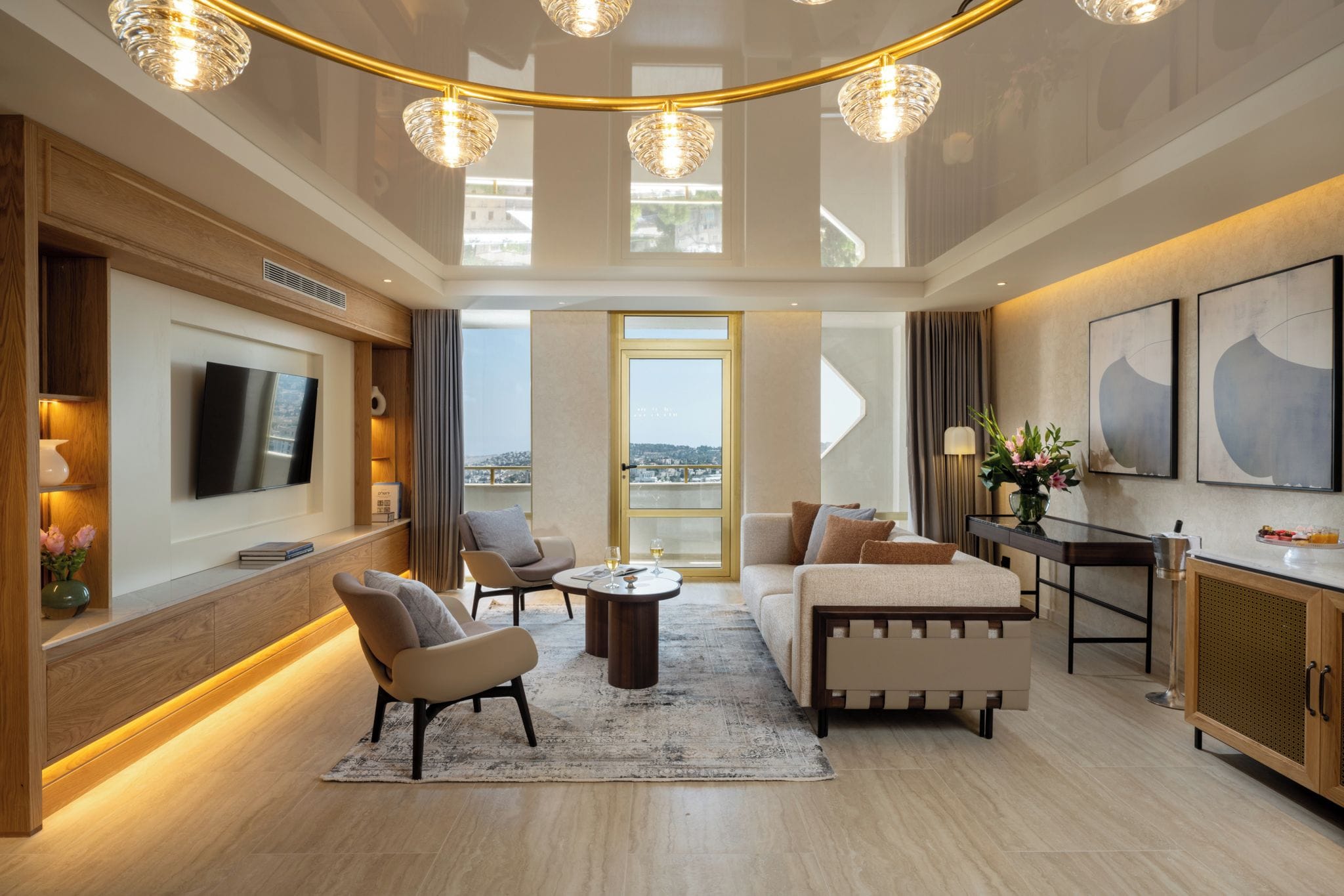 A modern living room with a flat-screen TV, comfortable seating, a dining area, and a view through a large window.