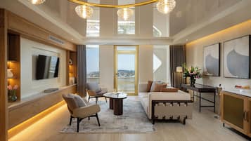 A modern living room with a flat-screen TV, comfortable seating, a dining area, and a view through a large window.