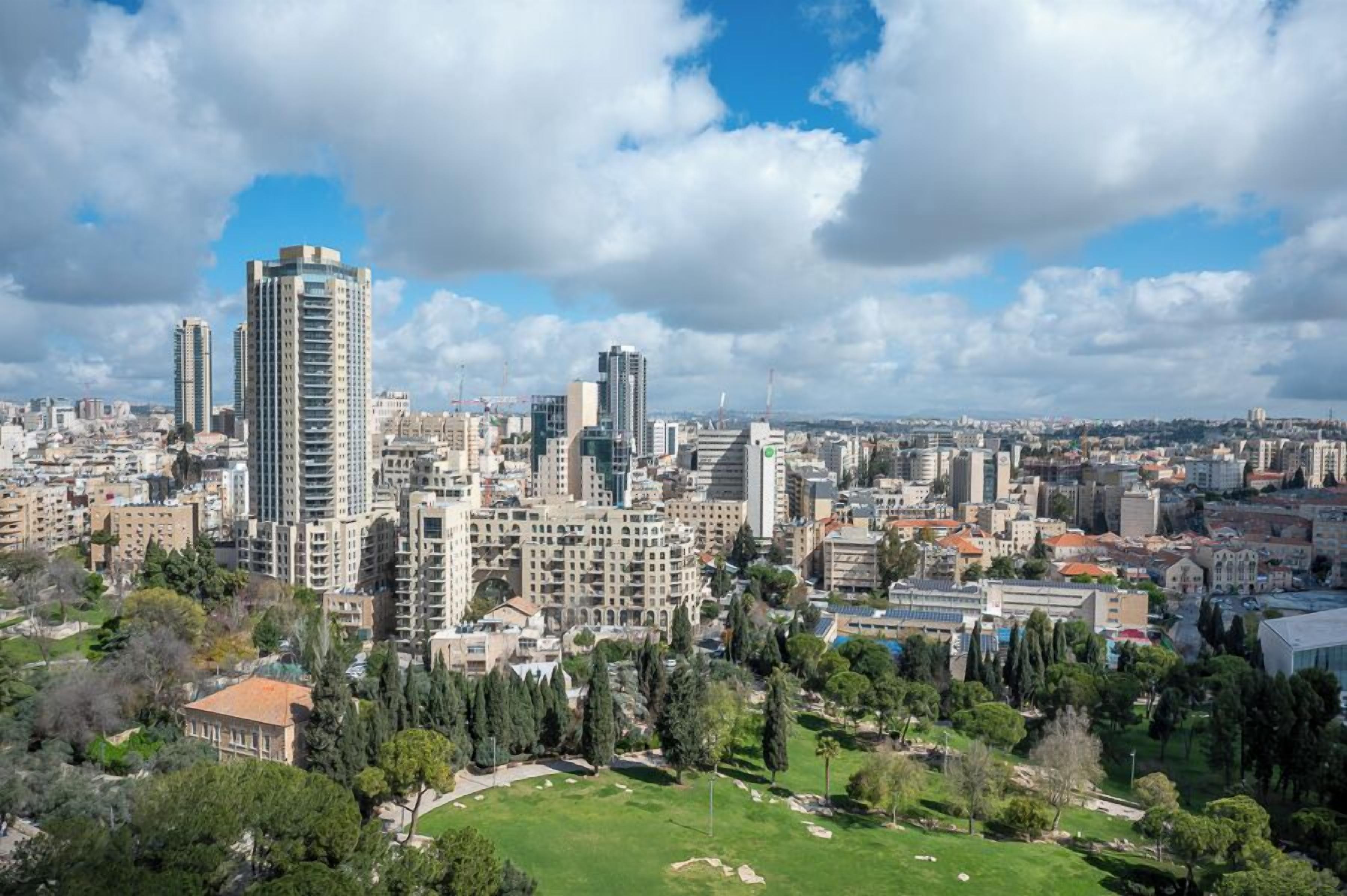 A cityscape with high-rise buildings, a park with greenery, and a clear sky.