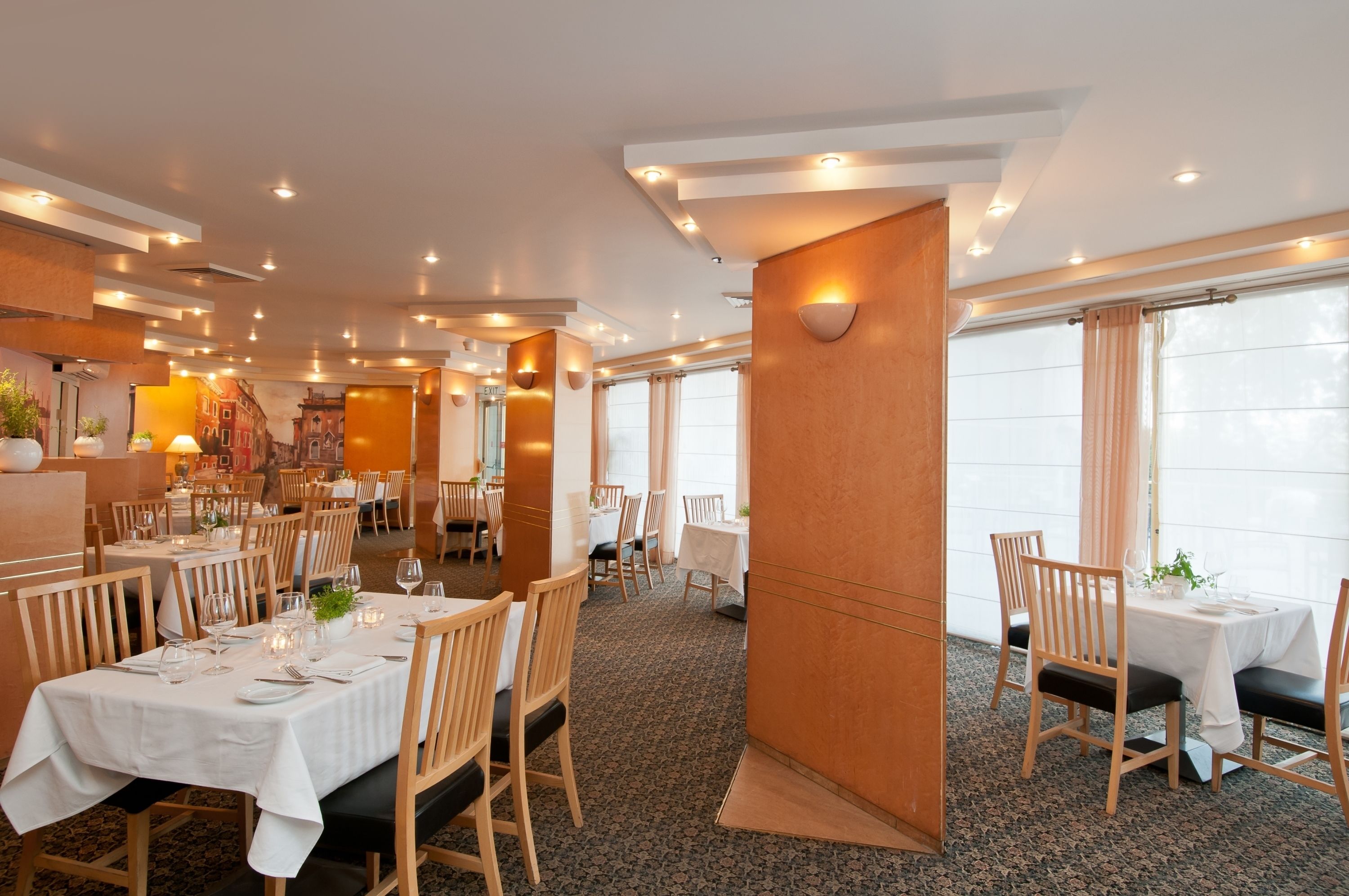 A restaurant with multiple tables, wooden chairs, and a carpeted floor.