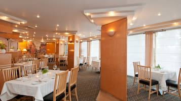 A restaurant with multiple tables, wooden chairs, and a carpeted floor.