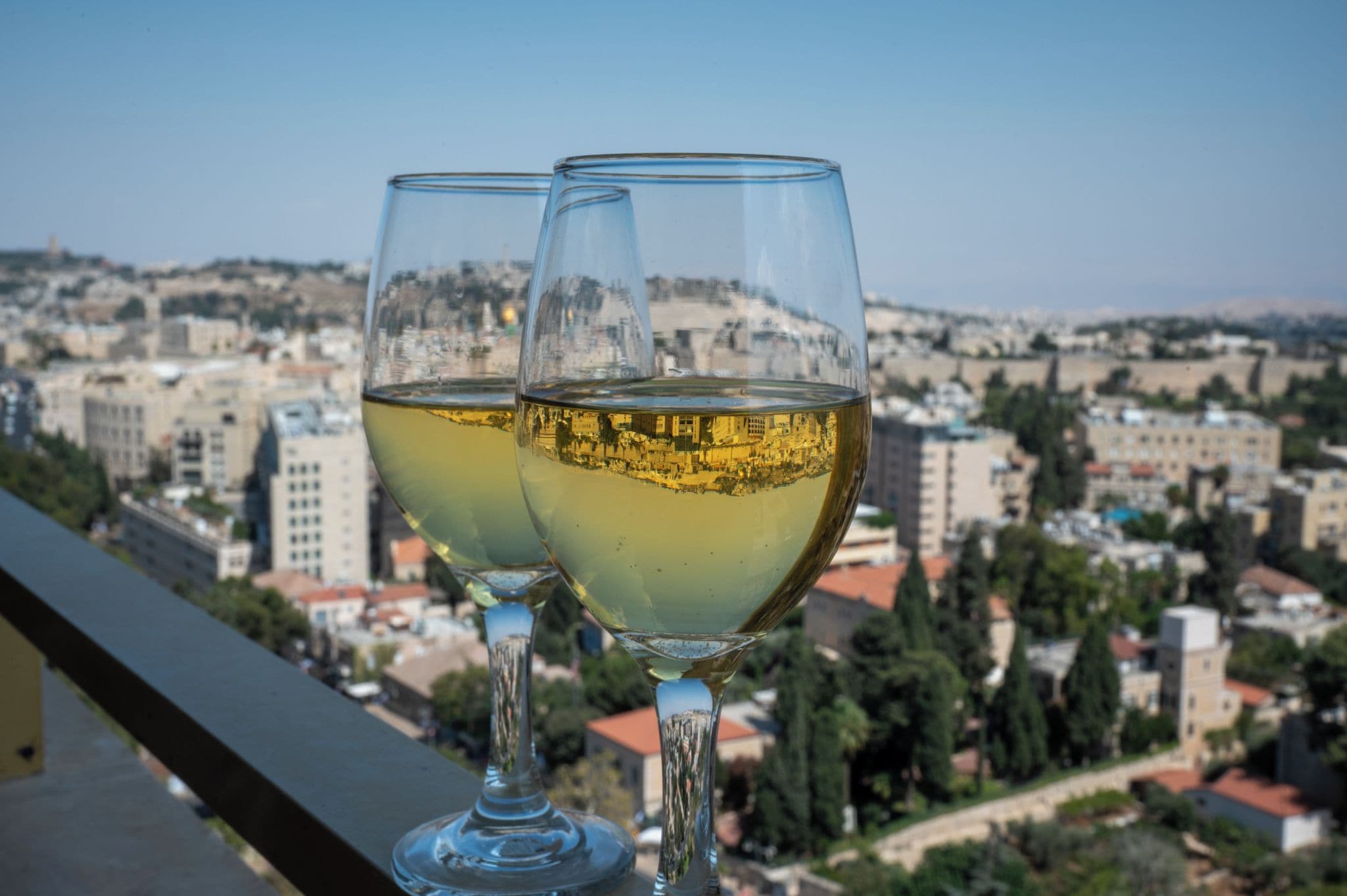 Dois copos de vinho branco numa varanda com vista para a paisagem urbana.