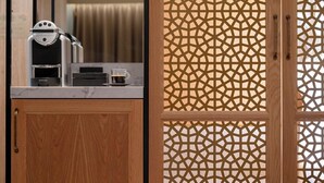 Un mueble de madera con una cafetera, una taza de café y una puerta mosquitera estampada.