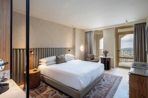 Habitación de hotel con una cama grande, mesita de noche, lámpara y vistas a través de un ventanal.