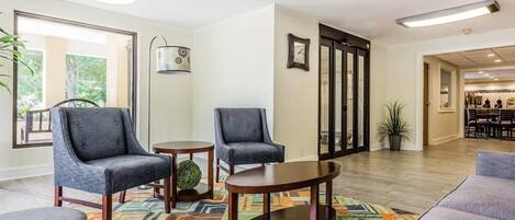 A modern lobby with two armchairs, a round table, a colorful rug, and a view of the dining area.